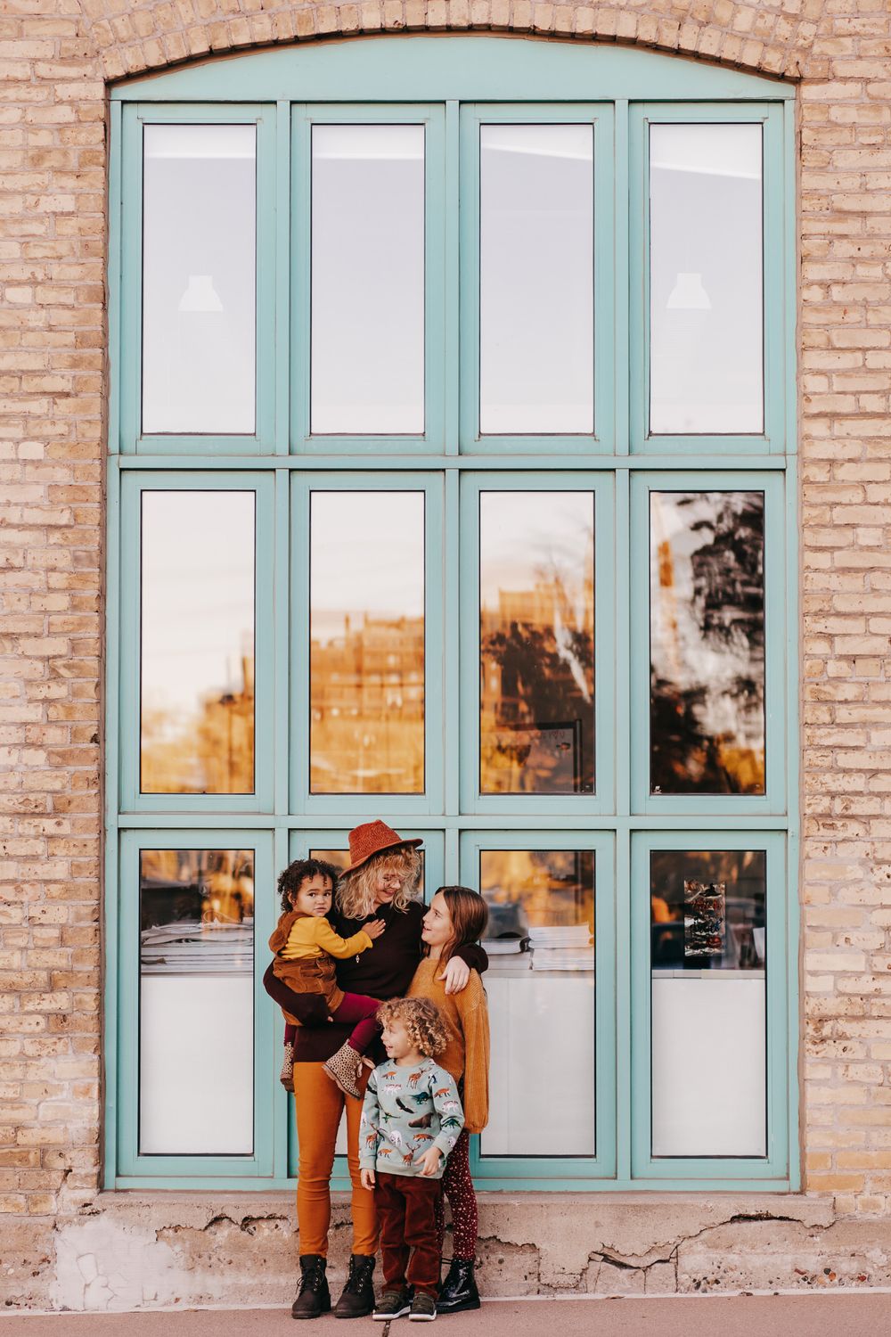 A mother and her three kids stand and laugh together in front of a teal-framed window in Minneapolis.