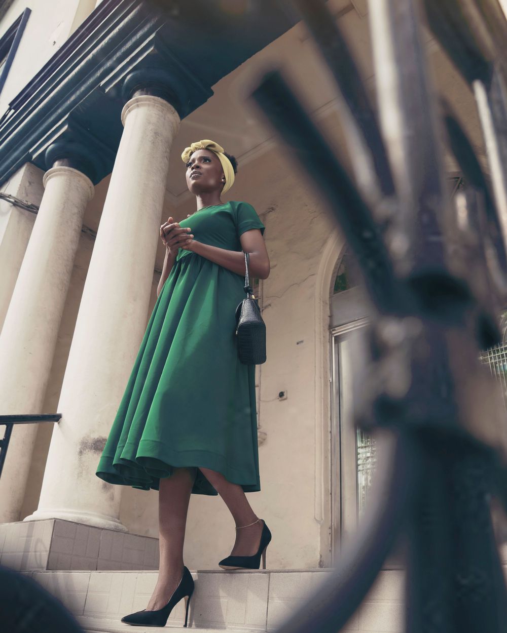 A low-angle shot of a woman in green dress standing among classical columns.