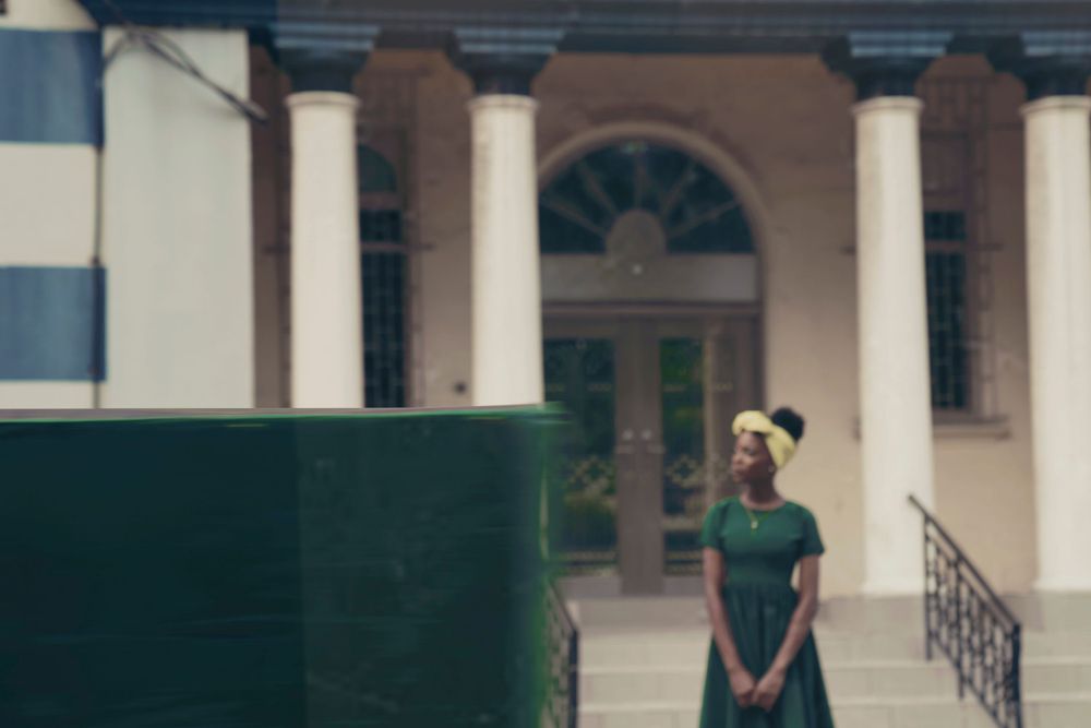 A dreamy portrait at a columned building featuring a forest green dress and yellow head wrap.