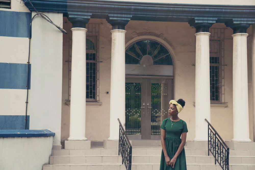 An architectural fashion photo featuring a green dress against a classical building facade.