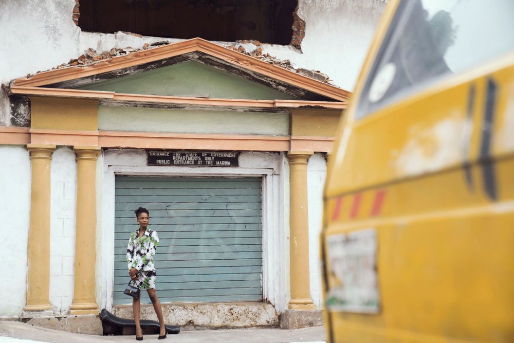 A street fashion shot with floral print dress against weathered yellow walls and shutters.