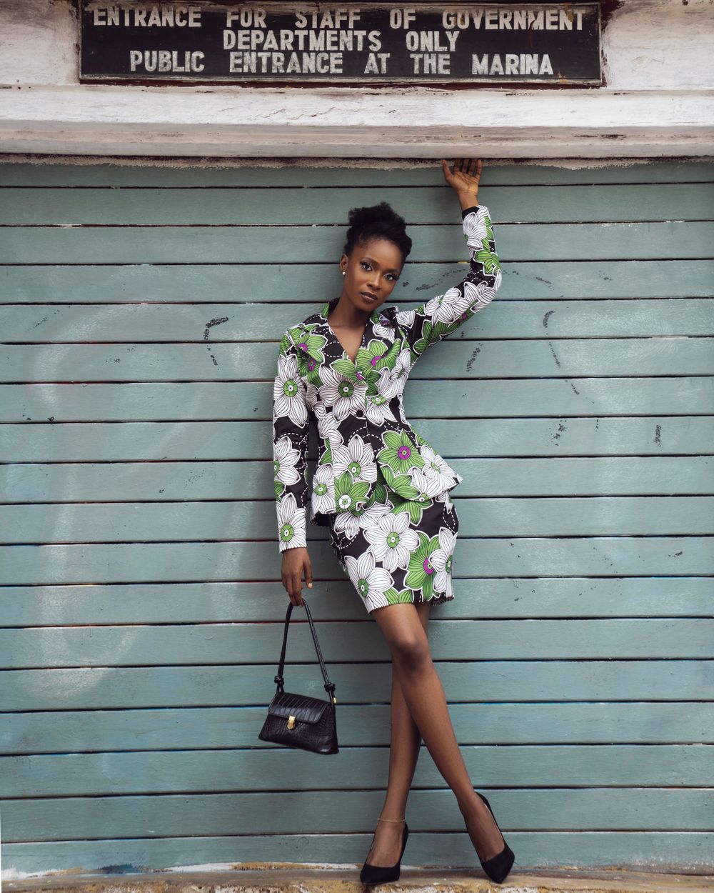 A fashionable floral dress pose against turquoise wooden doors at a government building entrance.