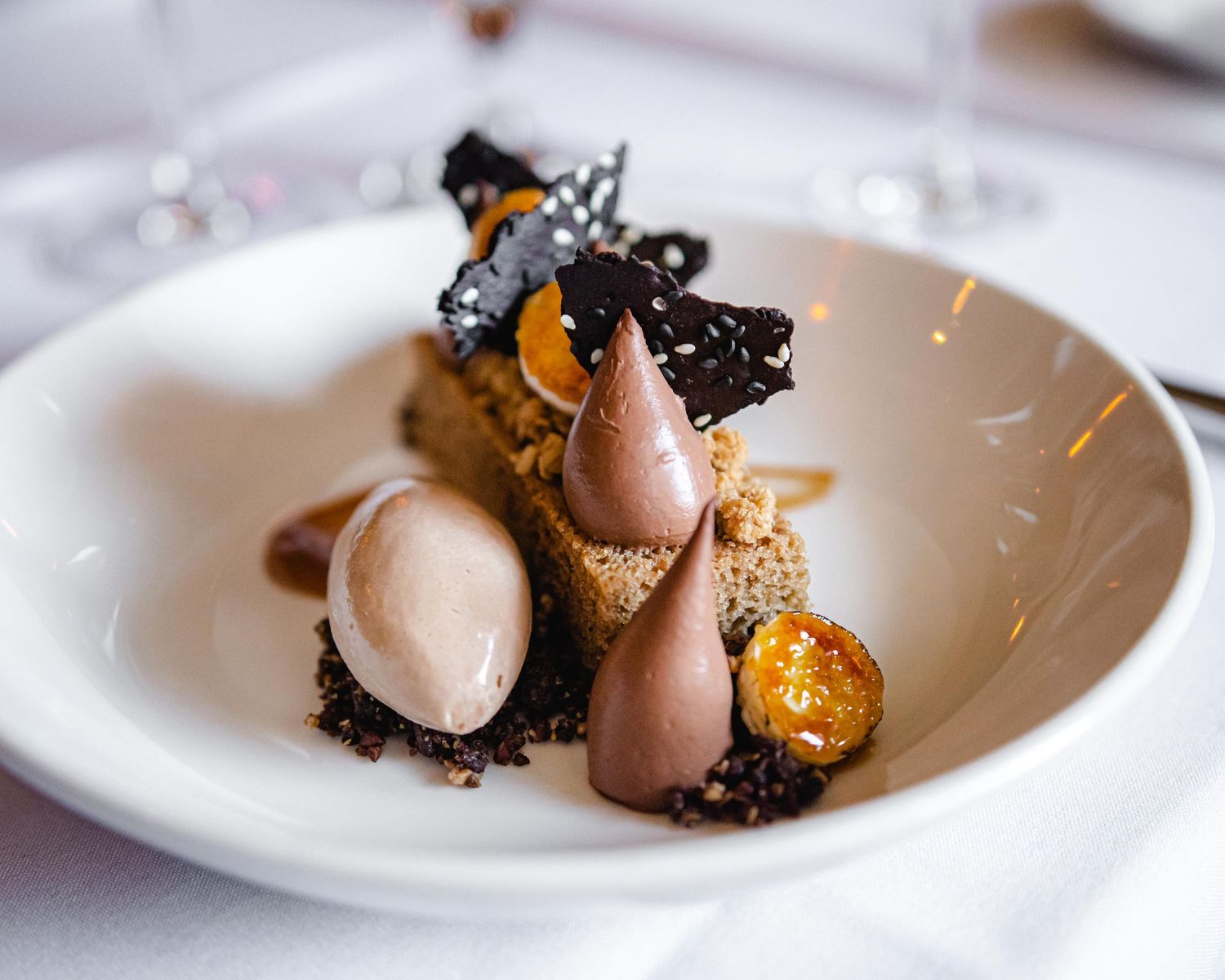 Gourmet chocolate dessert with truffle garnish, caramelized spheres, and cocoa crumble on white plate.
