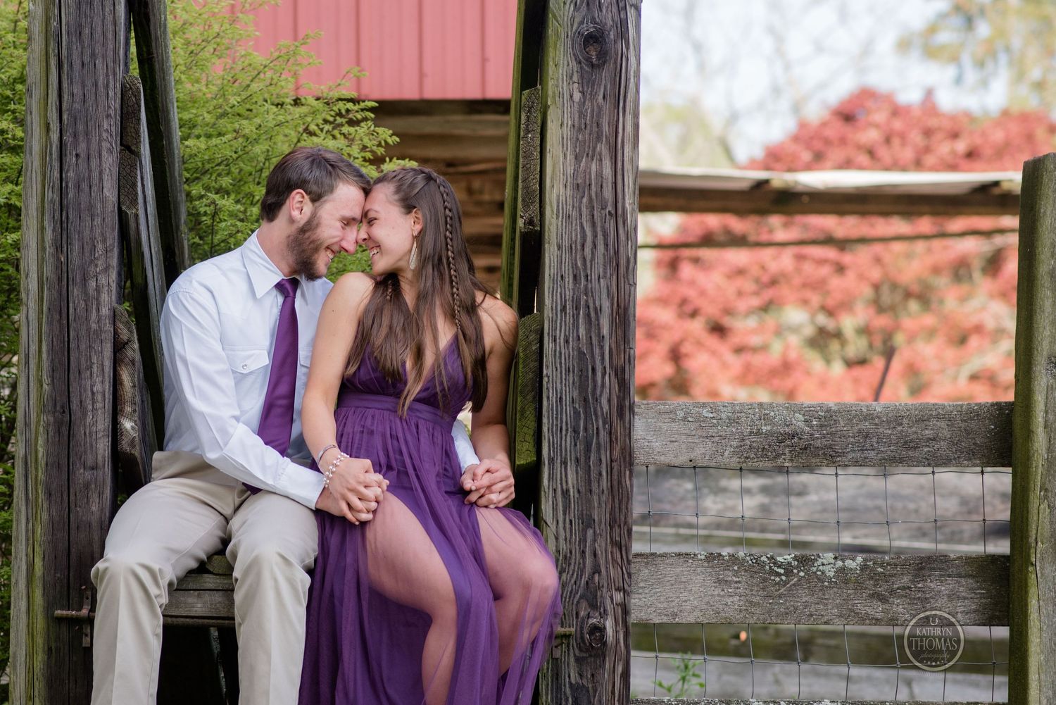 Couple in purple dress and white shirt share an intimate moment on rustic wooden steps at sunset.