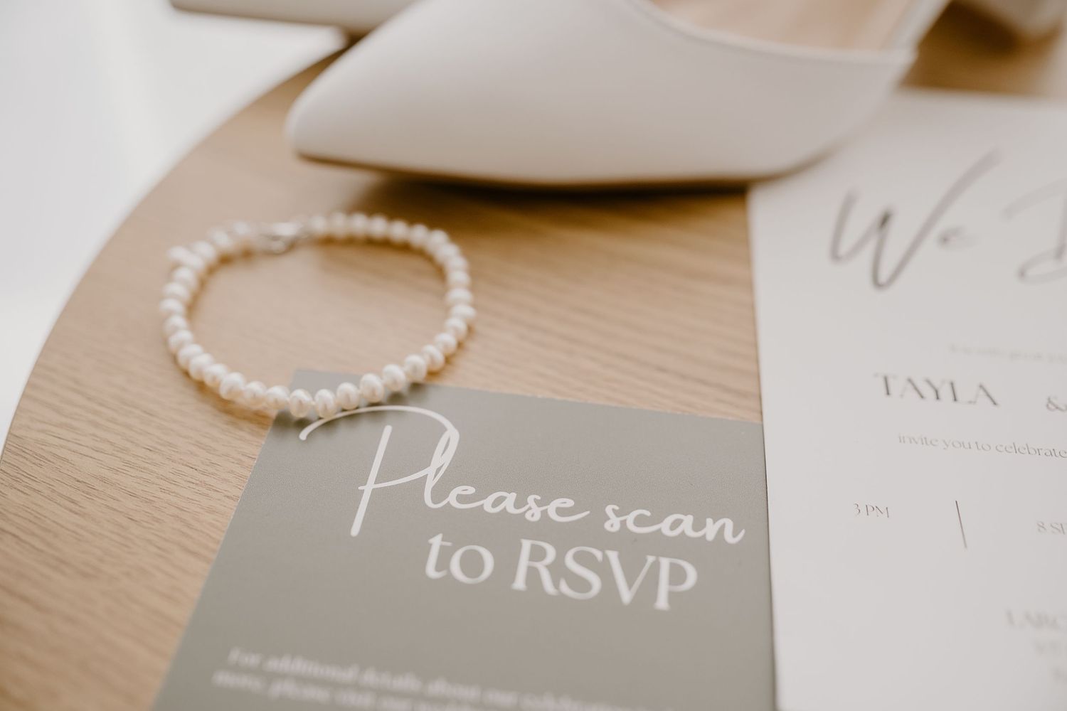 Wedding invitation RSVP card and pearl bracelet arranged on wooden surface.