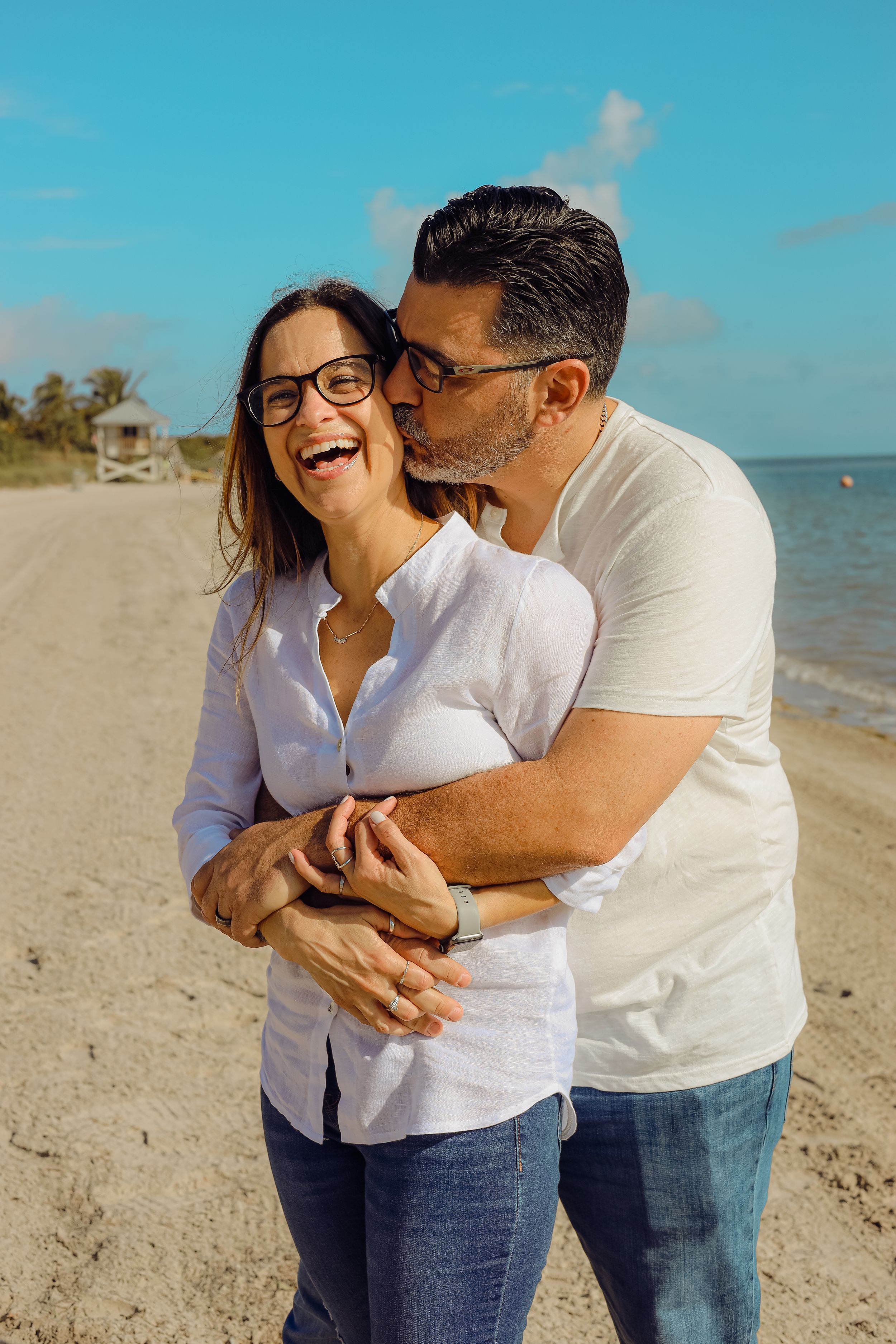 Romantic beachside moment between couple dressed in white against blue sky background.
