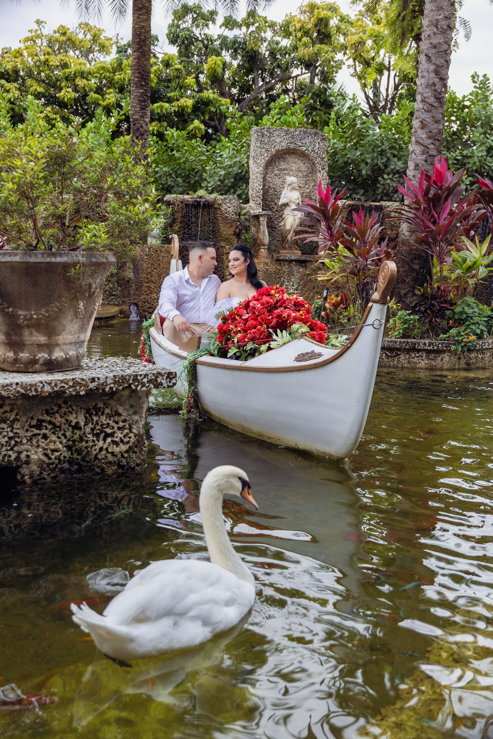 White canoe with red flowers in a garden pond with a graceful swan swimming nearby.