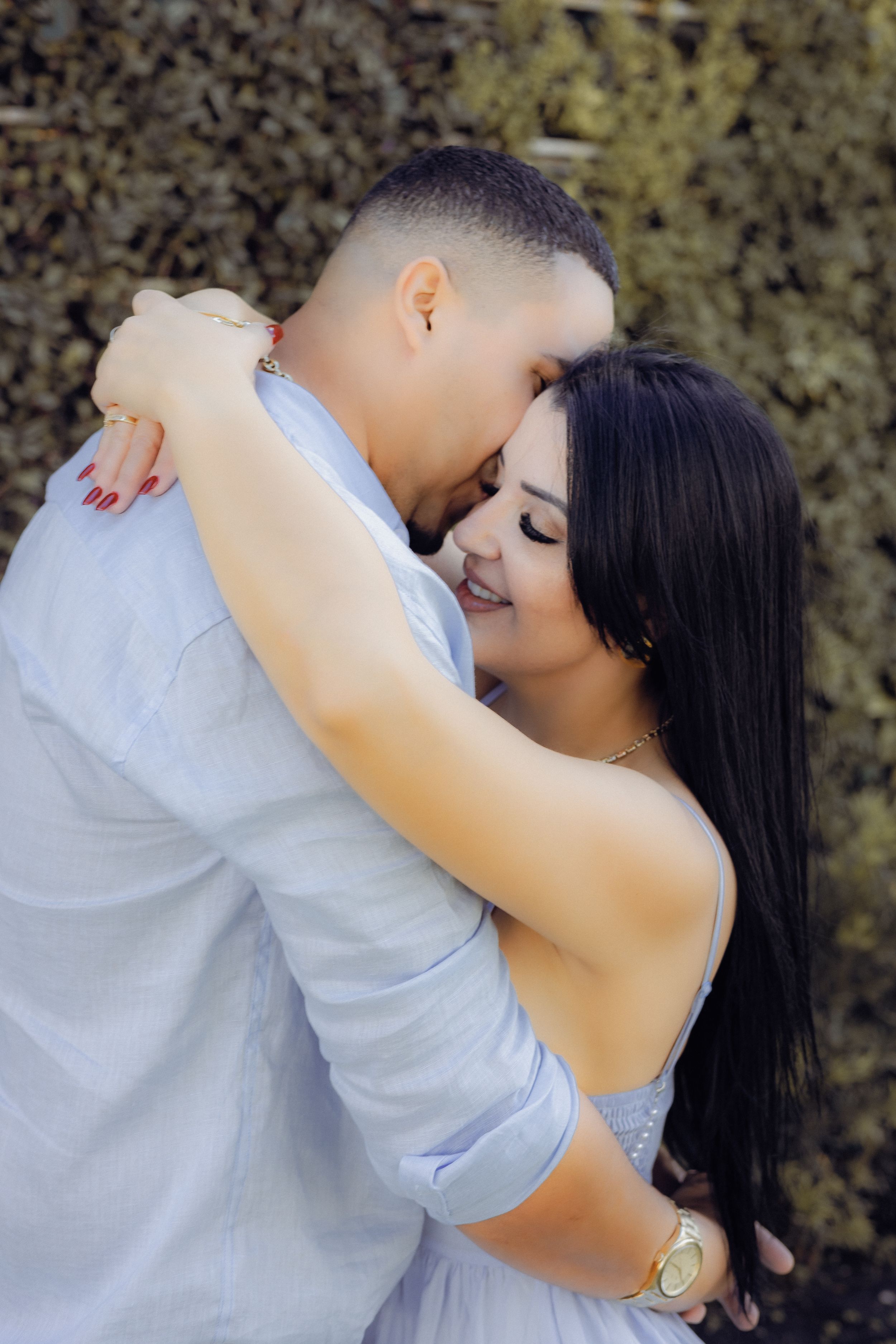 Intimate portrait of couple embracing in casual attire against a greenery backdrop.