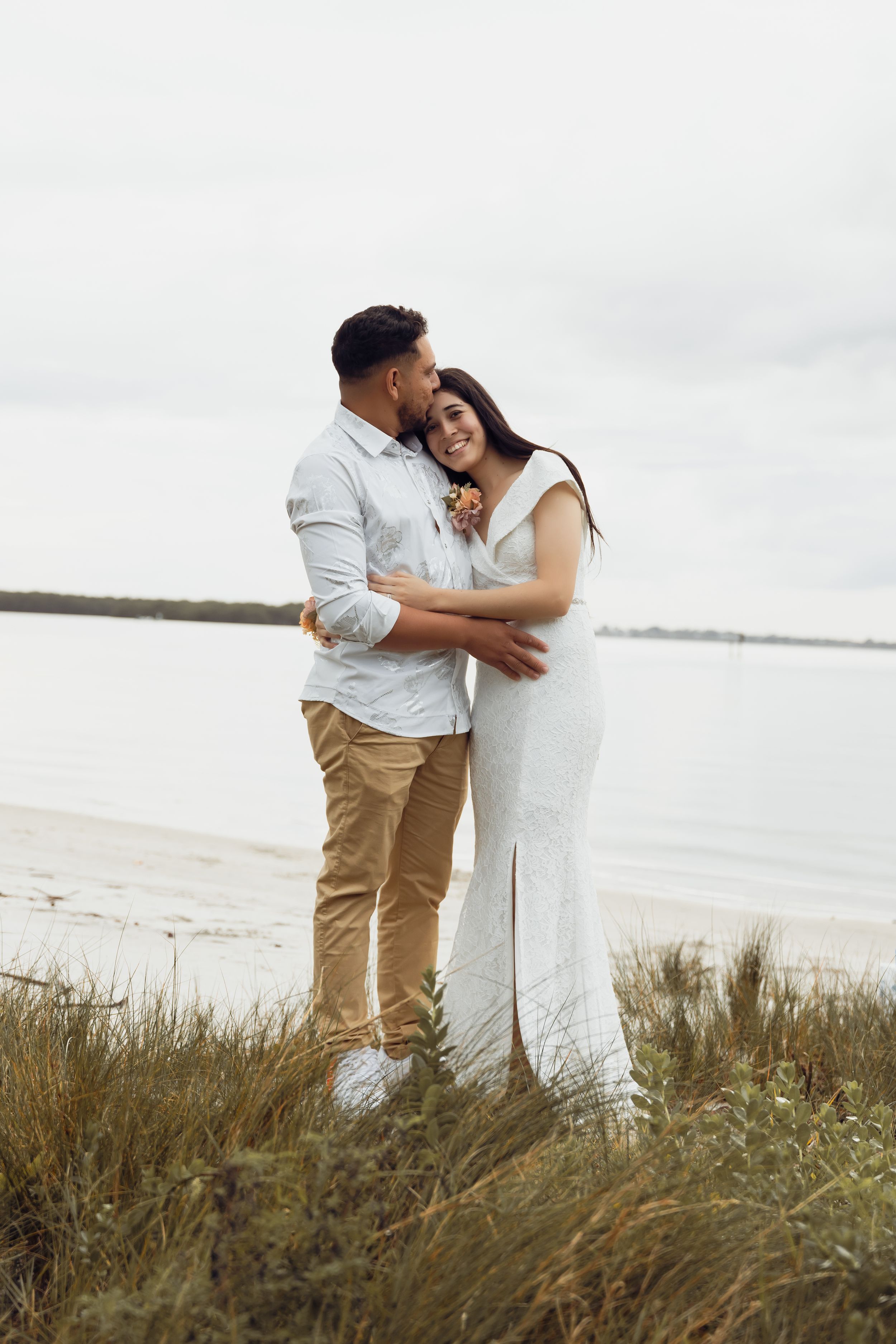 Romantic seaside portrait of couple in casual formal wear standing in coastal grass.