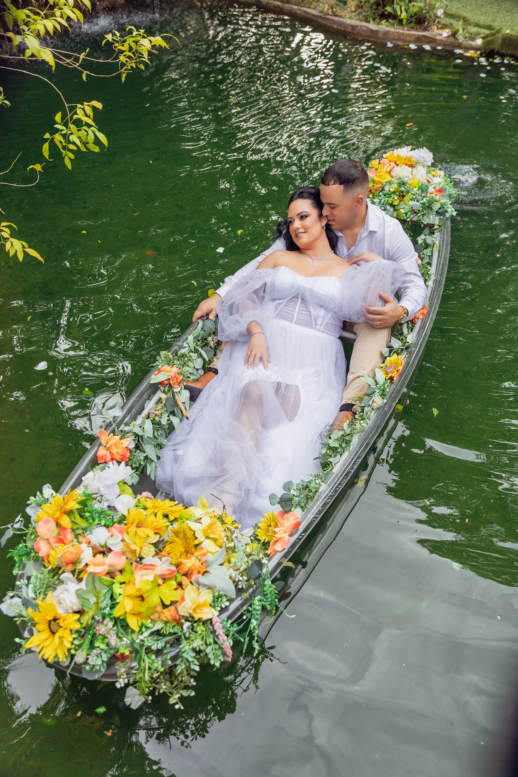 Decorated white canoe filled with colorful flowers floating on emerald green water.