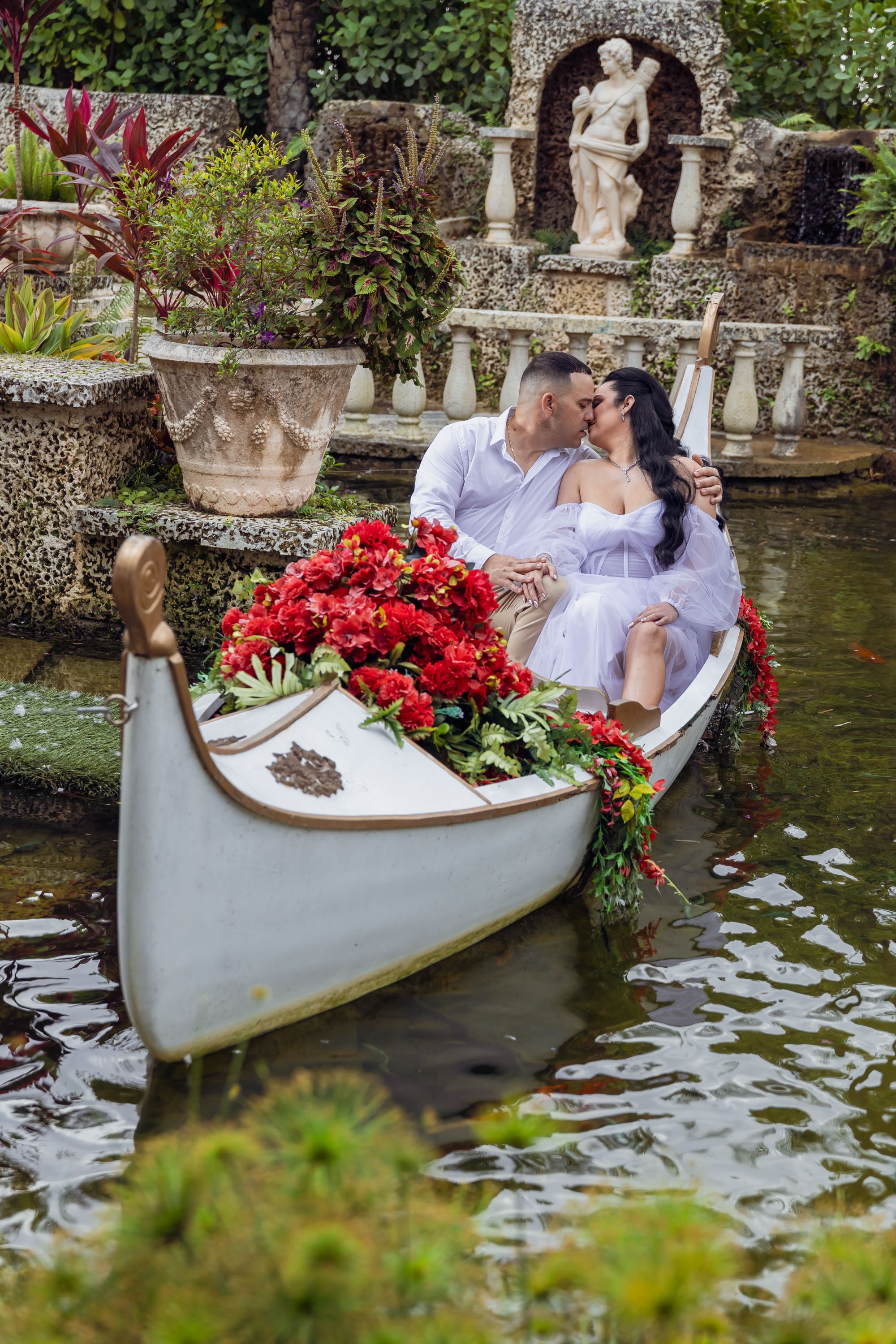 Romantic boat scene with red poinsettias and classical statuary in a garden setting.
