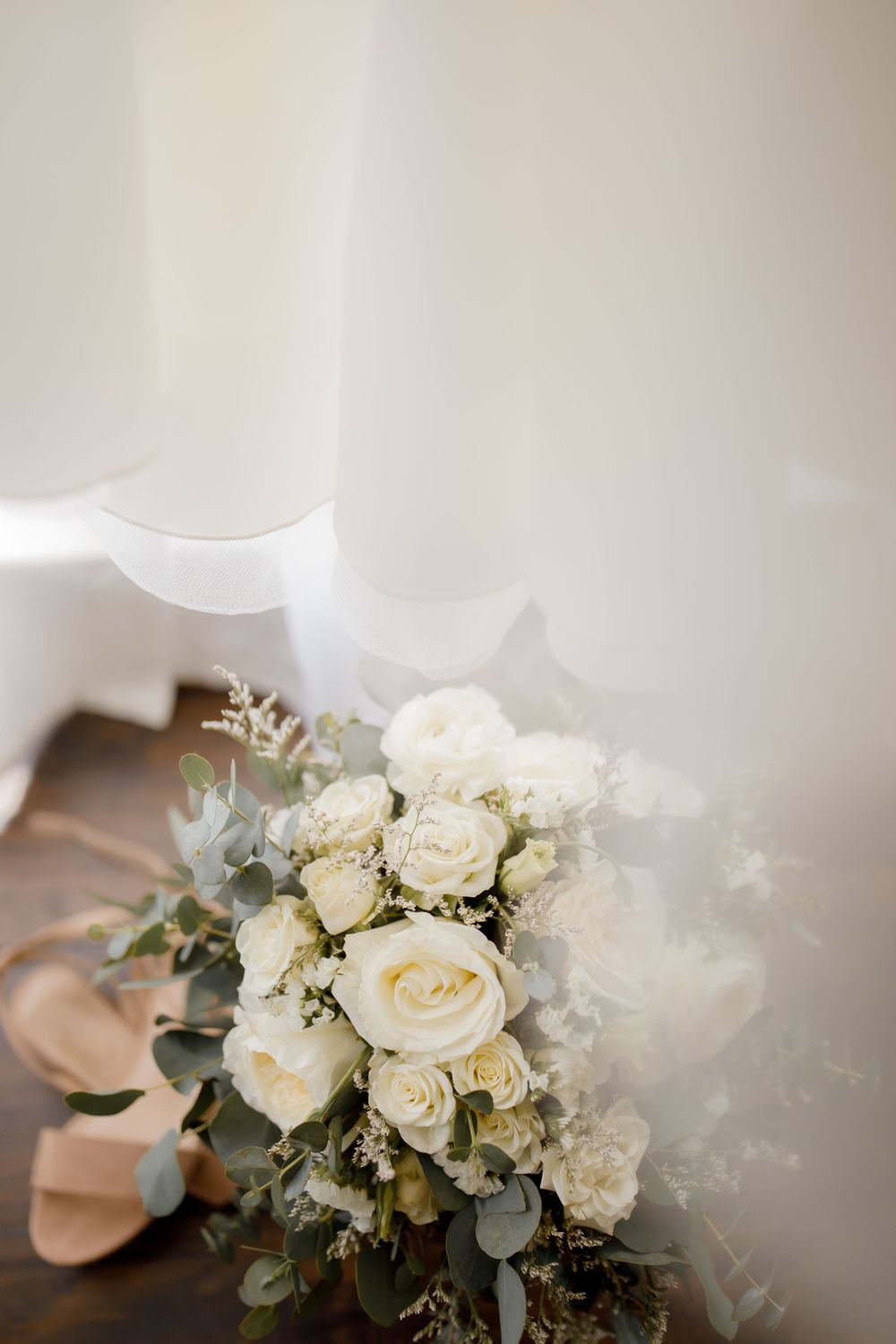 Elegant white rose bridal bouquet with eucalyptus leaves next to blush pink heels.