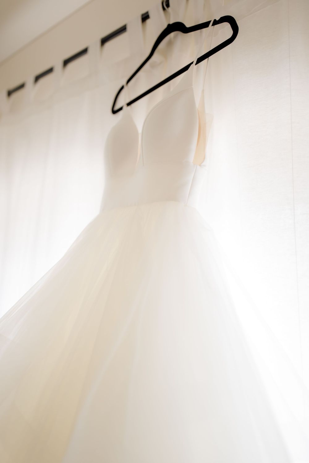 Ethereal silhouette of white wedding dress hanging against backlit window.