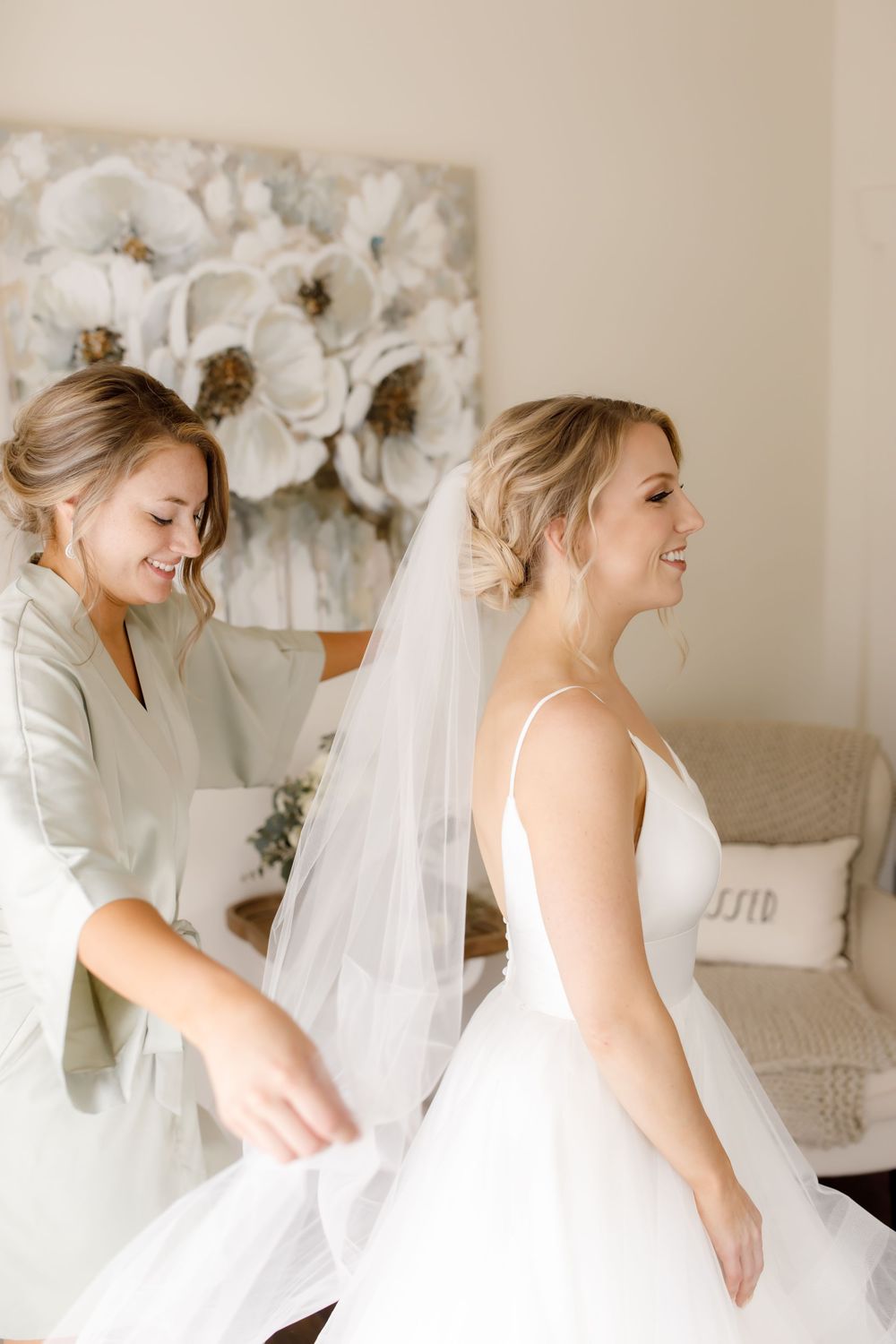 Tender moment during wedding preparation with white floral artwork in background.