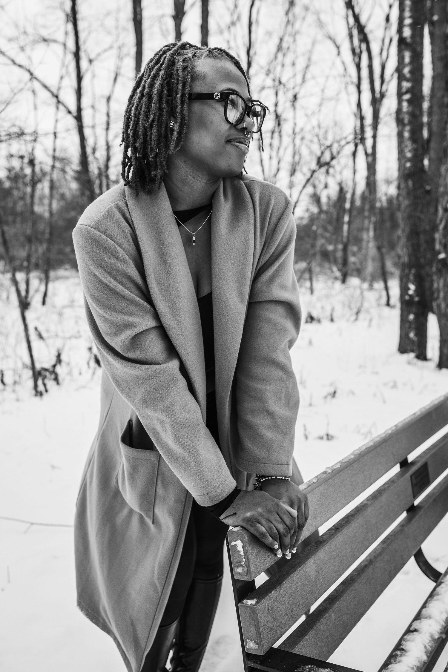 Black and white portrait in winter setting with beige coat and glasses.