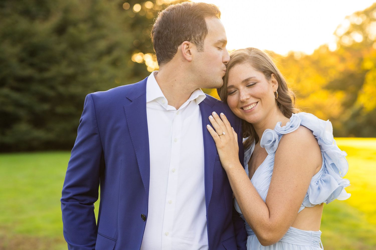 A couple shares a tender moment outdoors during golden hour in formal attire.