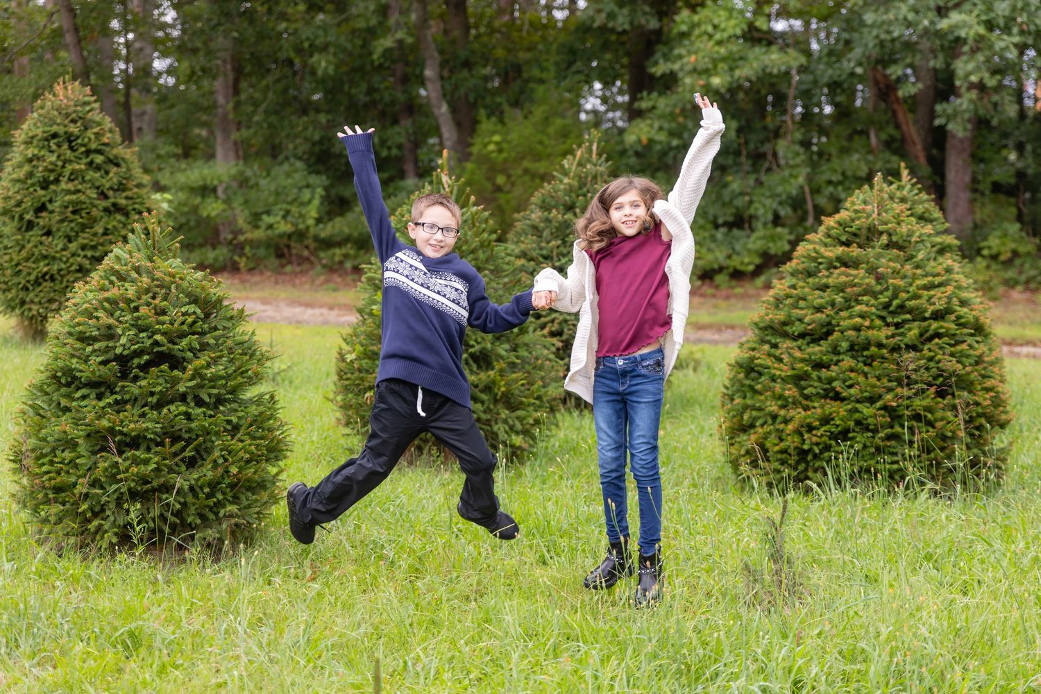 two kids jumping while holding hands in a christmas tree farm at turkey trac farms in millville new jersey cumberland