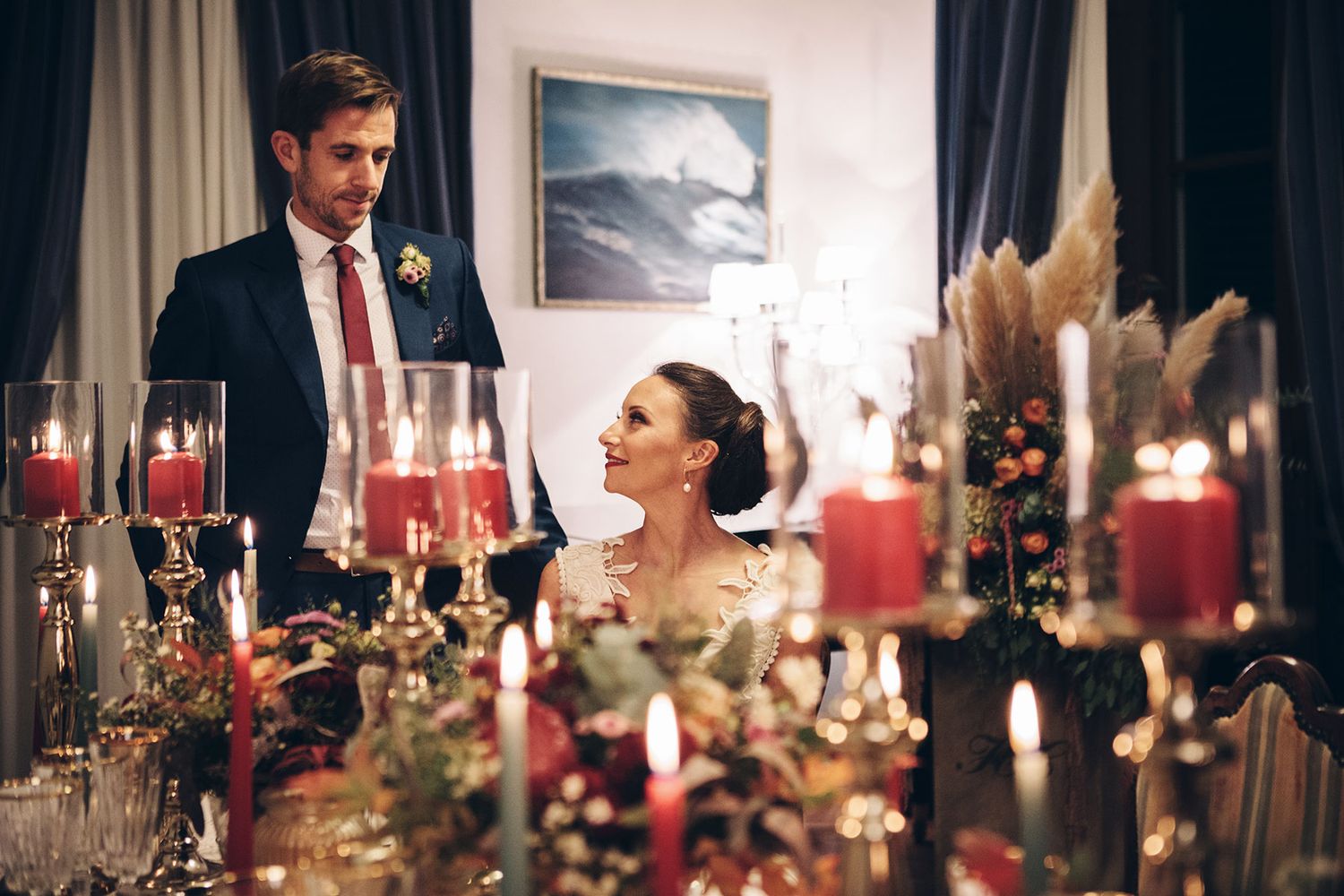 Elegant wedding reception dinner table adorned with glowing red candles and crystal glassware in a romantic setting.