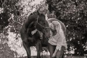 A black horse and its handler share a tender moment in a black and white photograph.
