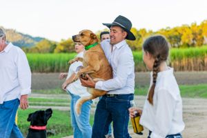 A dog being held on a rural path while others gather around during sunset.