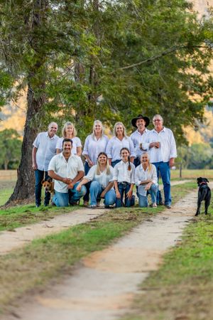 Group photo under a large tree on a dirt path with dogs and mountain scenery in the background.