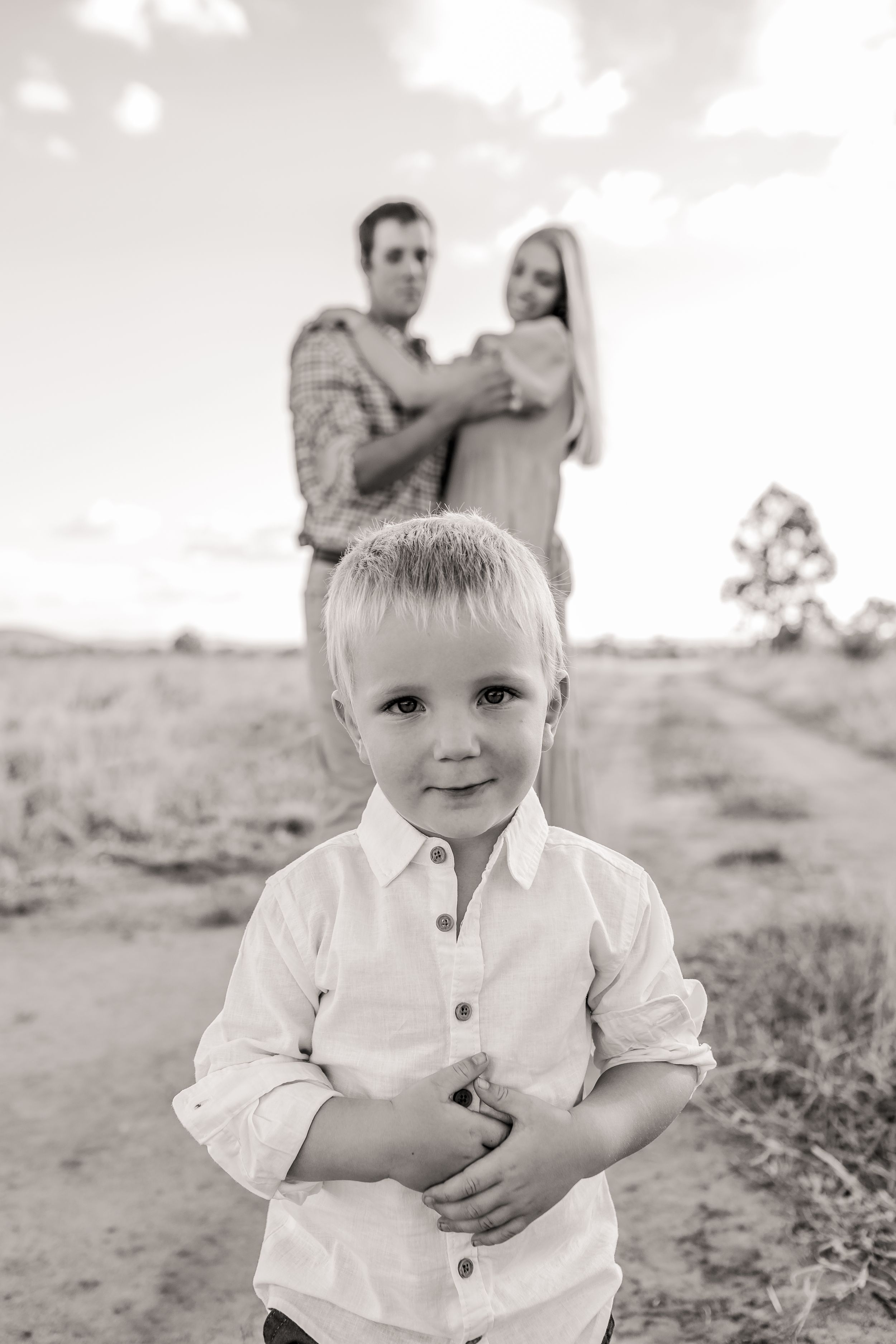 Young child in white button-up shirt standing in field at sunset.