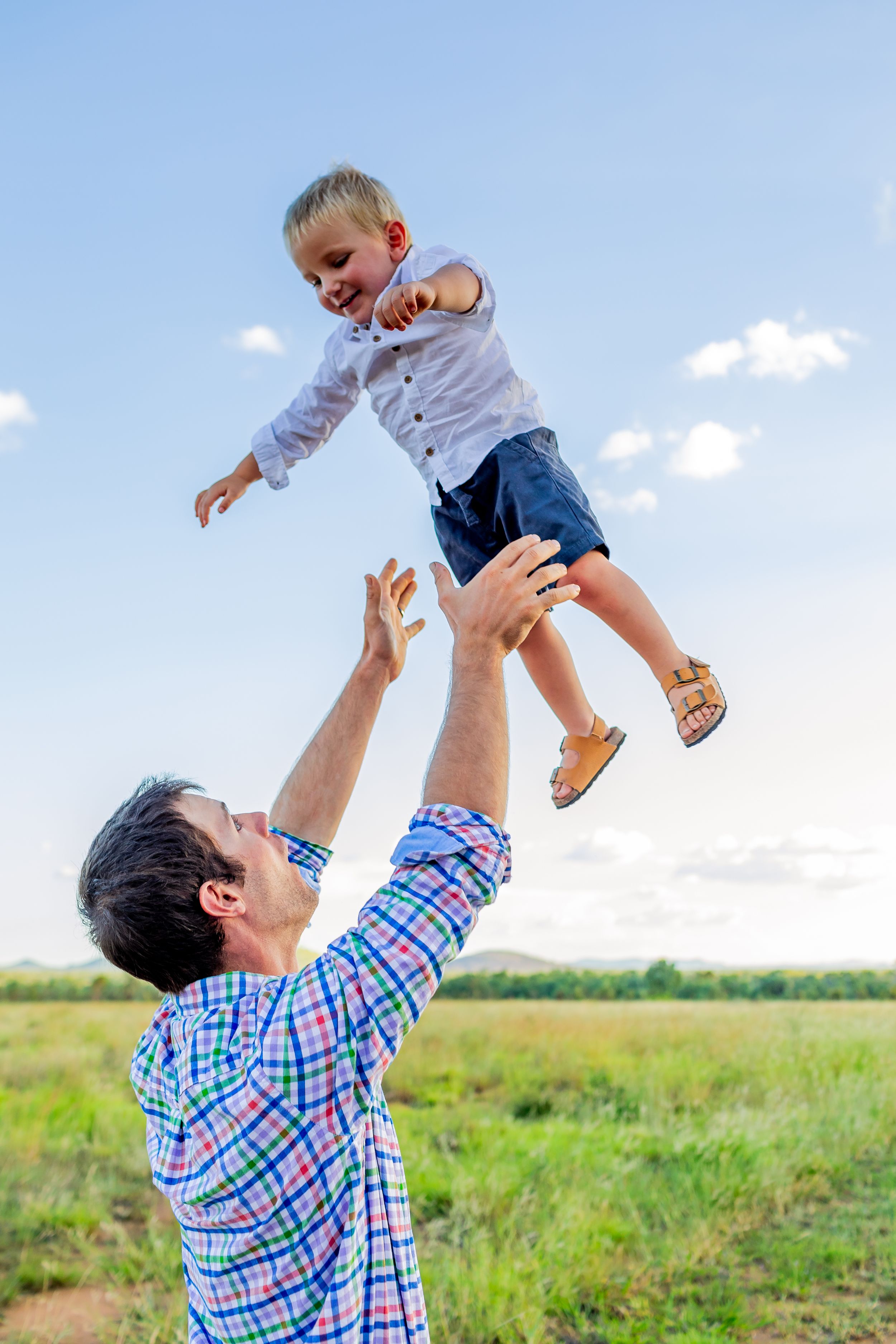Playful family moment with child being lifted in sunny field.
