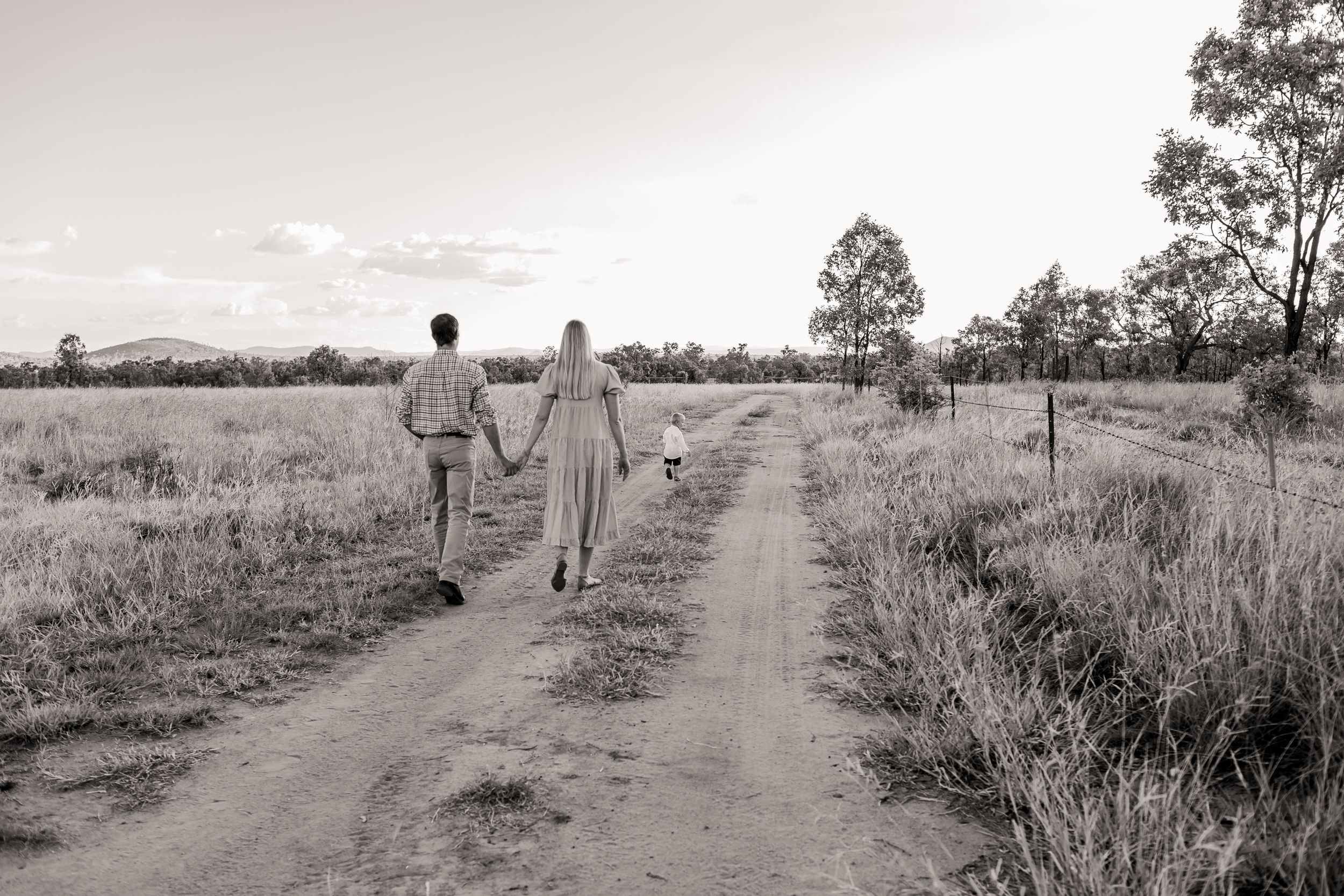 Black and white photo of couple walking down rural dirt path amid grassy landscape.