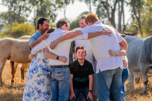 A group of people huddling together in fellowship outdoors with horses grazing in the background.