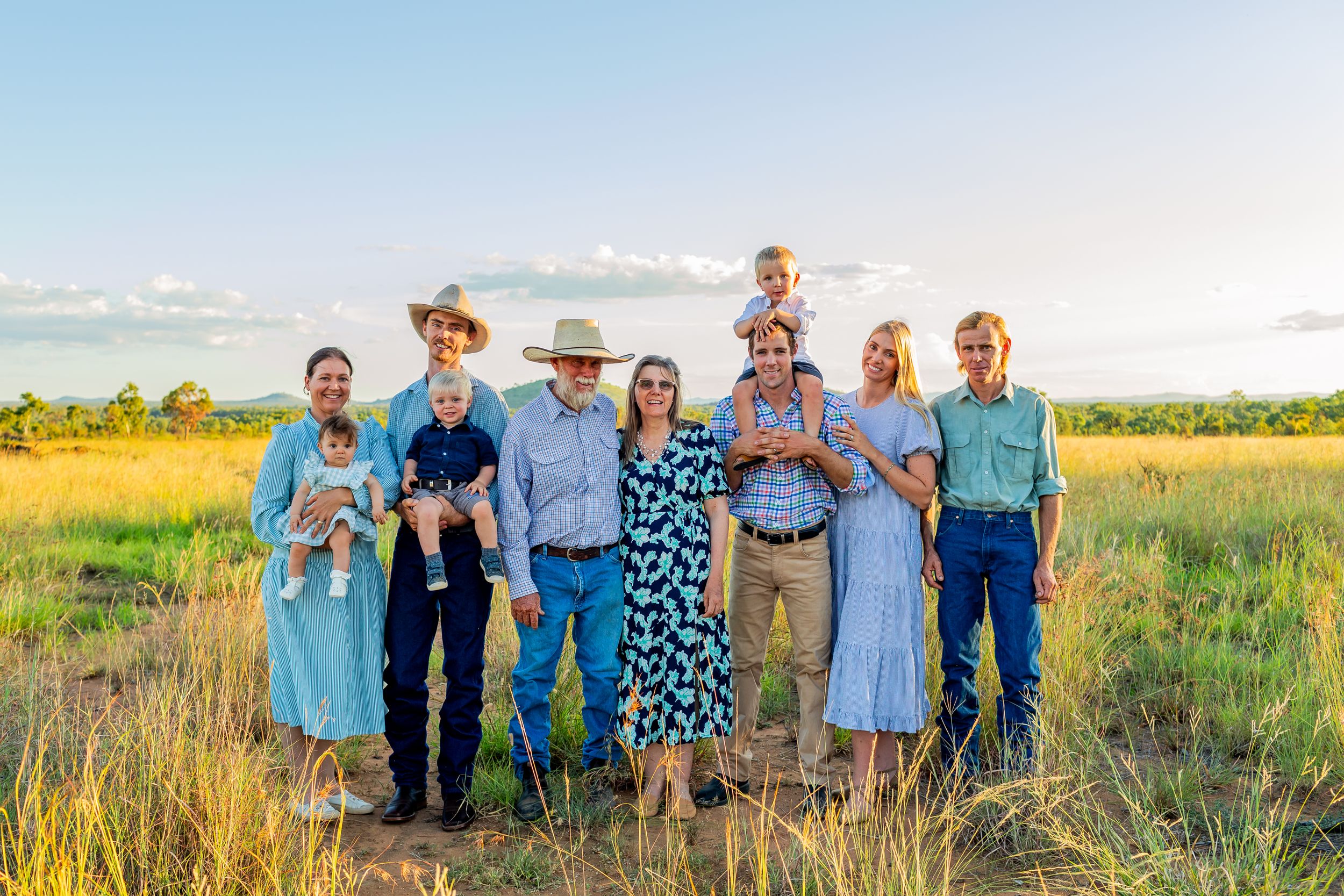 Group photo of extended family gathered in golden field at sunset.