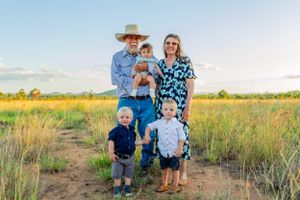 Family standing together with small dog in rural field setting.