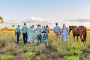 Group walking through field at sunset with horse following behind.