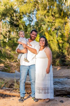 Family in coordinated outfits posing on a fallen tree trunk in a natural outdoor setting.