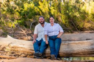 Couple sitting together on a large fallen log in a sunlit wooded area.
