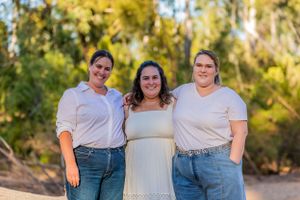 Three people in coordinating outfits pose together in front of golden trees.