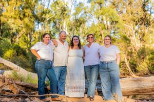 Group photo of family members in coordinated casual wear posed outdoors with trees in background.