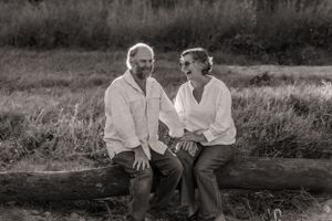 Black and white portrait of a couple sharing a laugh while sitting on a log outdoors.