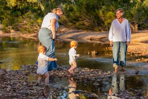 Adults and children playing and wading in shallow water by a riverbank during sunset.