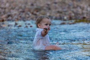A small child plays in shallow water among rocks during an outdoor photo session.