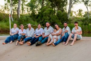 A casual group photo of people sitting together on the ground wearing coordinated white and blue outfits.