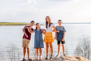 A group poses together on a rocky outcrop overlooking a scenic lake view on a bright sunny day.