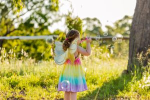 A rainbow dress catches sunlight as a child plays in a golden meadow during sunset.