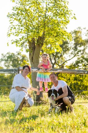 Family and their Border Collie enjoying a sunny day outdoors under a leafy tree.