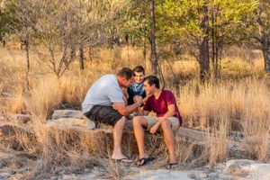 Three people share a moment together while sitting on rocks in a scenic outdoor setting.