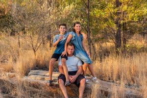 Three people pose playfully on a rock formation in a natural setting with dry grass and trees.