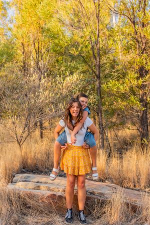 Two people enjoying a playful piggyback ride surrounded by golden autumn trees in a natural outdoor setting.