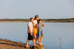 Three people standing together on a rocky shore with a peaceful lake in the background.