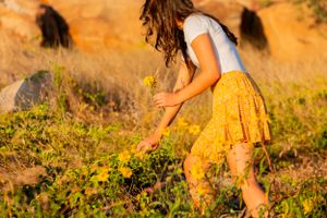 Person in yellow skirt walking through wild vegetation in warm sunlight.