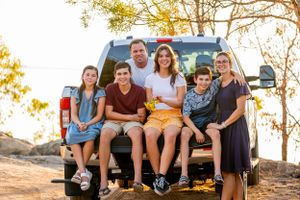 Group sitting on tailgate of pickup truck against backdrop of autumn trees.