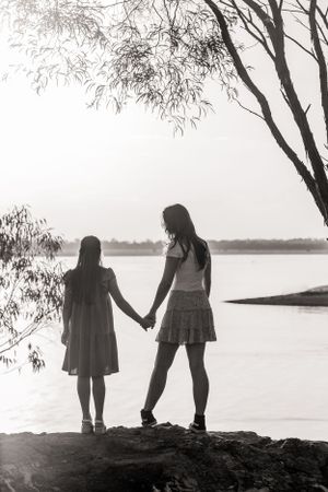 Silhouettes of two people holding hands while standing by a tranquil lake at dusk.